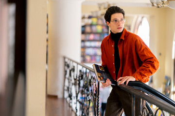 portrait of a young guy in glasses standing with a book in his hands in the library