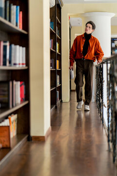 student walking along the corridors of the university library while studying looking at the shelves with books