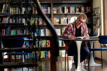 male professor in glasses sits in a scientific and technical library reads a book and prepares to...
