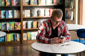 a man is sitting in a library cafe with a phone in his hands, looking for the title of a book he...