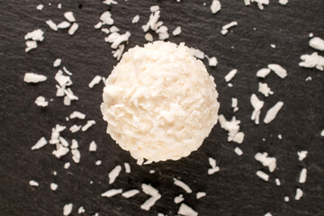 One candy with nut and coconut flakes on slate stone, macro, top view.