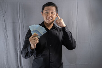 Young Asian businessman holding money with a happy gesture because his business and finances are on...