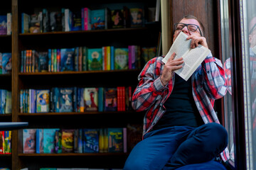 male professor in glasses sits in the library and laughs at the plot of the book against the...