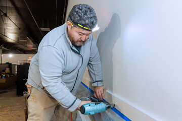 Contractor nails worker using an air gun during installation of wooden trim moldings at room