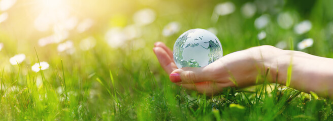 Woman hands holding a glass sphere of Earth on the green grass background.