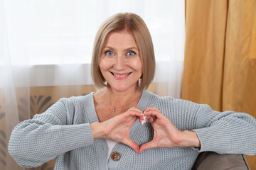 Blond senior woman relaxing, woman with heart made of hands, happy retirement and charity concept