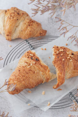 Fresh baked broken in half nut croissant on white paper closeup and dried flowers on retro metal baking rack on grunge stone table background.