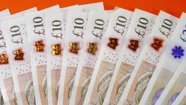 Closeup overhead pan shot of British sterling currency, with &pound;20 notes, &pound;10 notes and a solitary &pound;5 note.