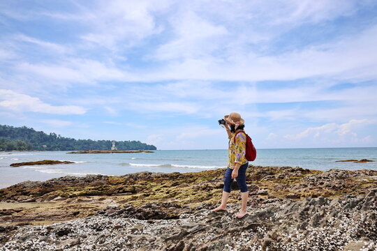 Tourists use digital cameras to take photos of the beauty of the sea and lighthouse in Phang Nga Province on hot summer day. Image of tourist wear wide-brimmed hat take photos in blue sky and sea
