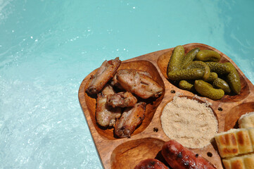 tábua com aperitivos , carne, pepinos , linguiçinha e pão de alho , fundo com  água da piscina 
