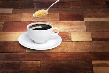 Spoon of sugar poured into a coffee mug with a white saucer on a wooden background.