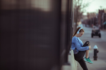 Young female athlete with headphones stretching in city street