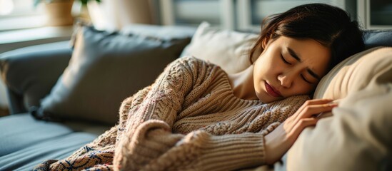 Asian young woman experiencing gastrointestinal discomfort, including food poisoning, stomach ache, and digestive issues, resting on couch at home.