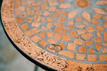 Fototapeta na wymiar Wedding rings lie on a round mosaic table