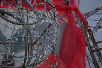 Metal silver-coloured heart hidden by metal rods and Christmas lights, partially covered with red, translucent, shimmering cloth