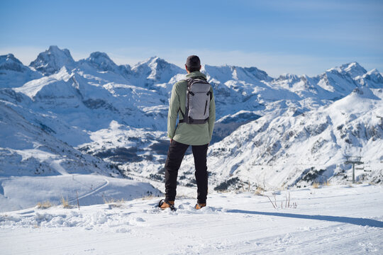 Hombre con ropa de monta&ntilde;a, mochila y raquetas de nieve en lo alto de la monta&ntilde;a mirando la cordillera nevada de la estaci&oacute;n de esqu&iacute; de Candanch&uacute; en los Pirineos Aragoneses.