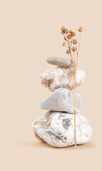 Tower of four stones, dry flax branch on neutral pastel beige background, front view, copy space, vertical format. Concept of harmony and balance, monochrome minimalist background. 