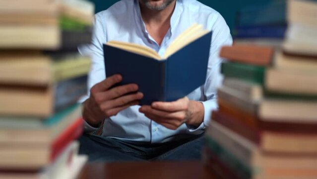 man reads a book - love of reading - man holds a book nestled among stacks of books in the library library