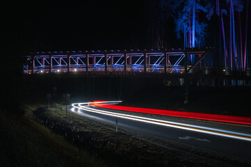 Colorful footbridge leading over a highway at night time. Light trails from car lighting up the road.  