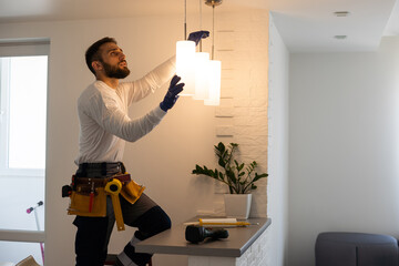Electrician installs lamp lighting and spot loft style on ceiling.