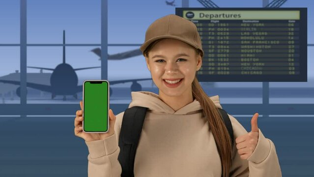 In the close-up shot of the airport with the waiting room. A woman in the foreground looks into the camera, smiles and holds the phone green screen to the camera. Advertising space