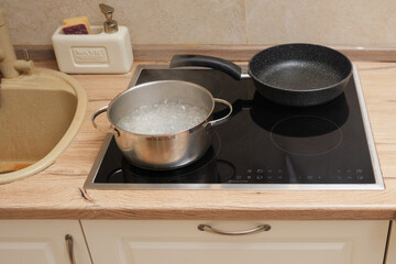 A pot of boiling water on a hot stove. Home beige kitchen with brown countertop and heated water on the hob