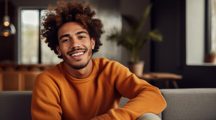 Portrait of a smiling man with curly hair wearing a rust-colored sweater, looking directly at the camera, with a warm and friendly expression