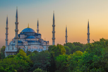 Obraz premium Beautiful view of a the Blue Mosque with towering minarets at sunrise, surrounded by lush greenery. Ideal for themes of culture, history, and spirituality in wall art, home décor, or educational mater