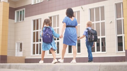 Fototapeta na wymiar back to school. a mother and children go to school with backpacks, rear view. school education learning concept. mother children with a backpack on her back lifestyle goes to school