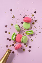 Creative Christmas and New Year composition with golden champagne bottle, confetti, pink and green macarons, pink background. Flat lay.