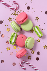 New Year composition with french green and pink macarons on pink background with confetti and Christmas canes. top view