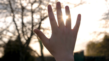 Silhouette of small child hand raised up to the sky, palm stretches towards sunset, sun shines...