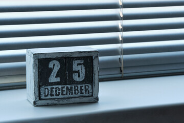 Morning December 25 on wooden calendar standing on window with blinds.