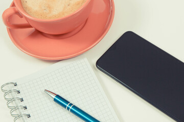 Mobile phone, coffee with milk and notepad for writing notes. White background