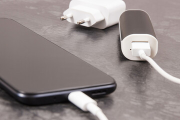 Black smartphone with connected plug of external powerbank. Mobile phone charging