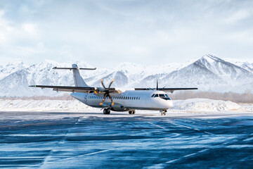 White passenger turboprop airliner on the winter airport apron on the background of high...