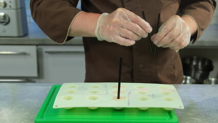 Obraz na płótnie Canvas Creative male culinarian puts plastic straws in mold with pate. Restaurant chef about to serve meat balls in form of lollipop