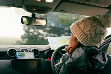 Latin woman leaning on the steering wheel while checking her cell phone and a map to check the route to follow on her trip through Ireland - Powered by Adobe