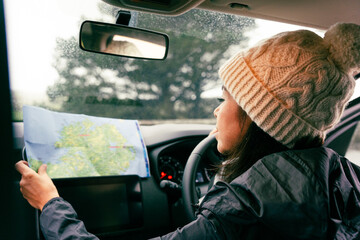Woman with knit hat inside her car seen from behind while checking her cell phone and map to find...
