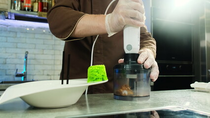 Man in uniform blends ingredients with mixer in kitchen. Chef uses professional electric devices...