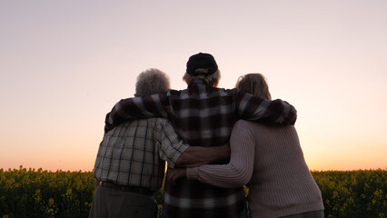 Meeting of elderly parents and adult female daughter. Family hugs standing in rural field and sees...