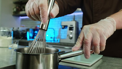 Chef holds stewpan by handle while mixing ingredients with whisk. Man cooks delicious dishes for...