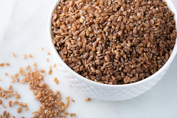 Close up of wheat grains in bowl on marble background. Healthy food concept.