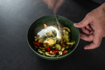 Asiatischer Gurkensalat in der zubereitung auf dunklem Hintergund in dunkler Schale Hände beim...