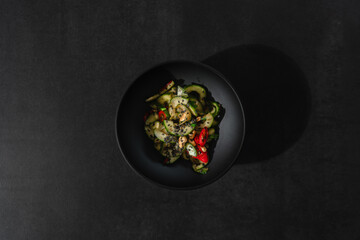 Asiatischer Gurkensalat auf dunklem Hintergund in dunkler Schale