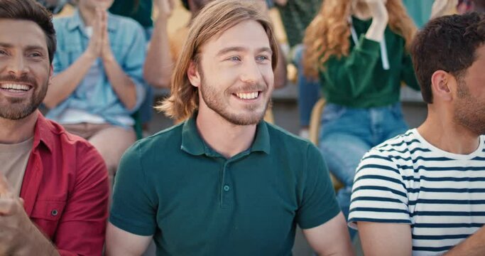 Happy fans watching soccer event at stadium. Handsome men sitting next to each other and cheerfully congratulating team with goal scored. Crowd making standing ovation at stadium.