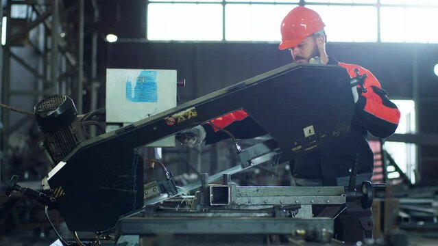At industrial factory worker using heavy machinery to cut off the metal in front of the camera he wearing safety equipment and helmet