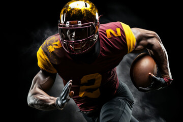 Portrait of American football player running with the ball. Muscular African American athlete in a burgundy and yellow uniform with an ovoid ball in a dynamic pose. Isolated on black background.