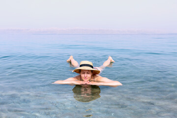 Woman with hat relaxing in salty water of a Dead Sea