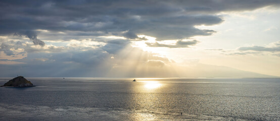 Sunbeams pierce through the clouds, casting a divine light over the sea with a solitary islet